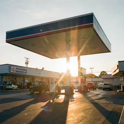 A gas station canopy rim-lit by the setting sun with lens flare