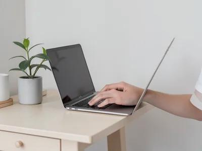 Hands typing on a slim laptop at a standing desk, plants and minimal decor