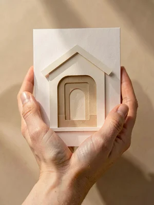 Papercraft brand-card of layered paper-cut hands cradling a paper-cut hall, soft