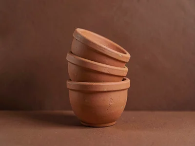 Catalog shot of a stack of terracotta pots in three sizes against a deep clay co