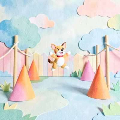 Playful cut-paper scene of a backyard with cones, weave poles, and a jumping pup