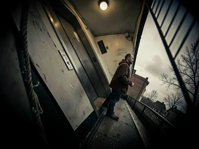 Man waiting for an elevator that won't come, the hallway tilted like a sinking s