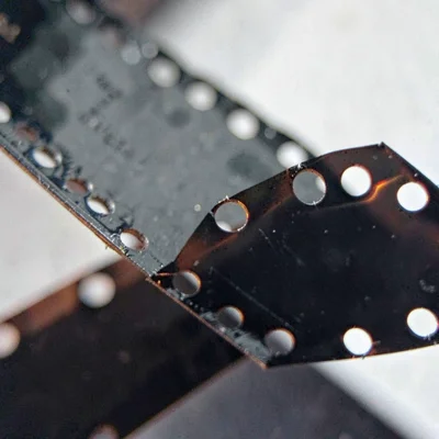 Mineral-cut close-up of perforation holes along a 35mm film strip, edge curling 