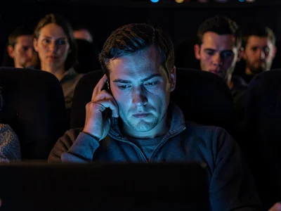 Person on phone in movie theater, the antisocial glow, sidelong glares from neig