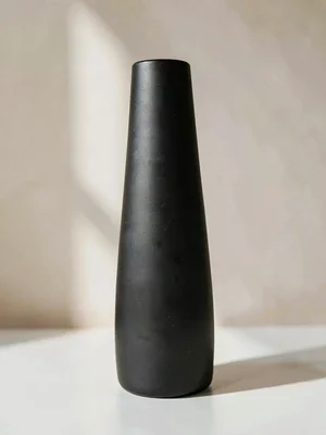 The sleek ceramic vase in matte black contrast stands tall showing a tapered cyl