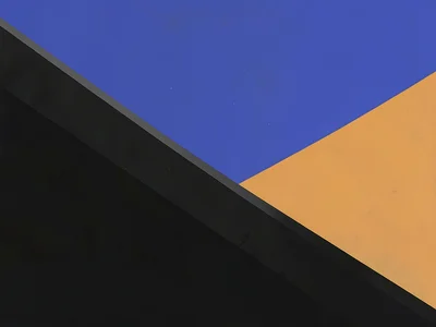 Diagonal blacktop crosses an ochre plateau beneath a vast lapis sky, hard mid-da