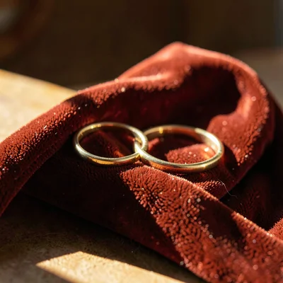 Warm still-life of two simple gold bands resting on a folded velvet ribbon, raki