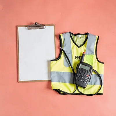 Catalog still of a clipboard, two-way radio, and folded high-vis vest on coral b