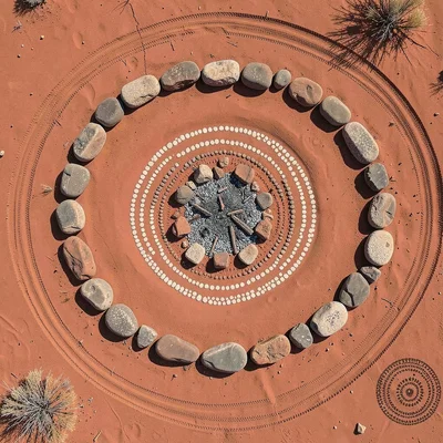 Desert campfire circle of stones on red sand from above, ash at center
