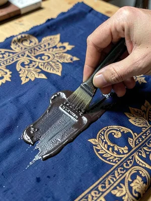 A hand scraping hardened wax off a finished cloth, the indigo cloth beneath appe