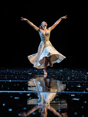 A dancer on wet stage floor, reflection completing their form
