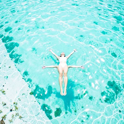 Expansive turquoise negative space, bleached whites, A woman floating on her bac