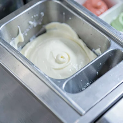Macro of a stainless gelato batch freezer with cream visible in the chute, miner