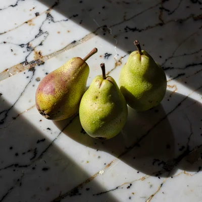 Three pears arranged on worn marble, afternoon light from left, long shadows