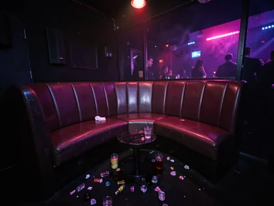 Empty nightclub booth at 4am, spilled drinks catching the still-running lights, 