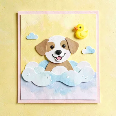 Cut-paper collage of a smiling dog in a bubble bath with floating rubber duck, s