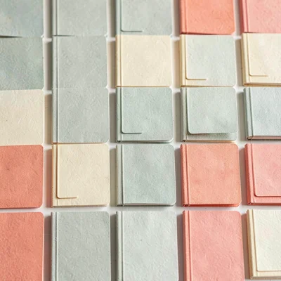 Papercraft pattern of repeating paper-cut notebooks in soft sage, coral and butt
