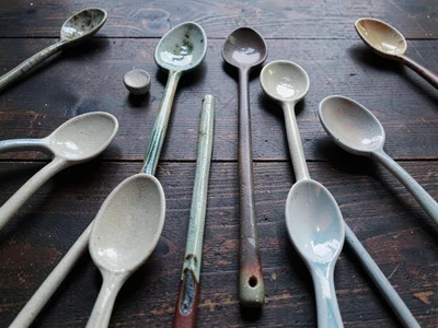 A collection of ceramic spoons in varying ash glazes spread on a dark wood surfa