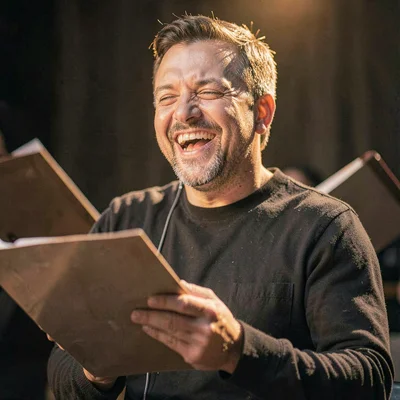 Portrait of a VO performer laughing mid-take, hand on script, soft fall-off