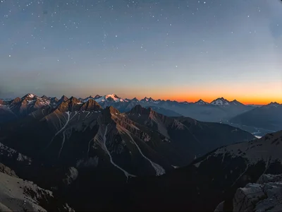 Alpenglow on distant peaks while upper sky shows faint stars