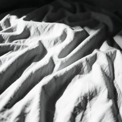 A crumpled bedsheet in morning light, the folds creating a landscape of shadow a