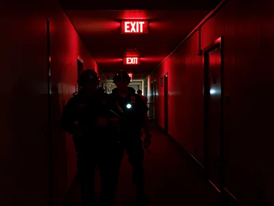 Night security patrol under red glow, flashlight off, navigating by exit signs a