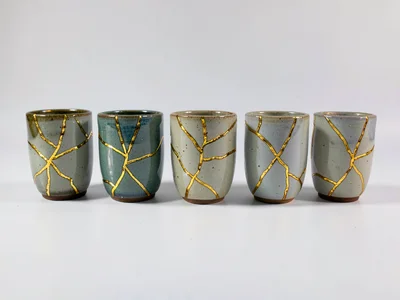 Series of repaired ceramic cups in a row — each with unique crack constellation