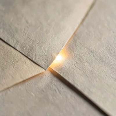 Two paper tongues meeting at a sharp diagonal seam, a single bead of light runni