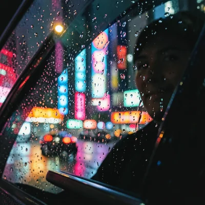 Rain on taxi window, neon city lights smeared into abstract color, passenger ref