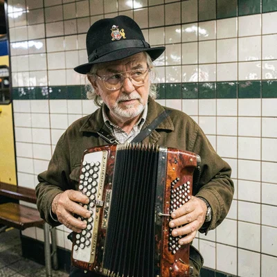 Subway busker with accordion, tiles gleaming behind, plastic lens adding soul