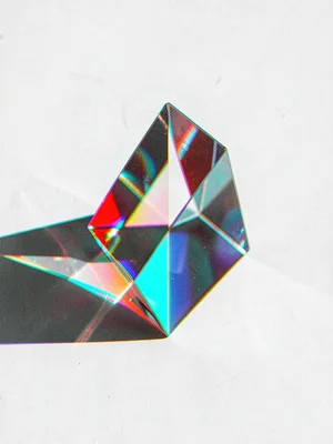 A glass prism splitting light on a white surface, the prism body strongly fringi