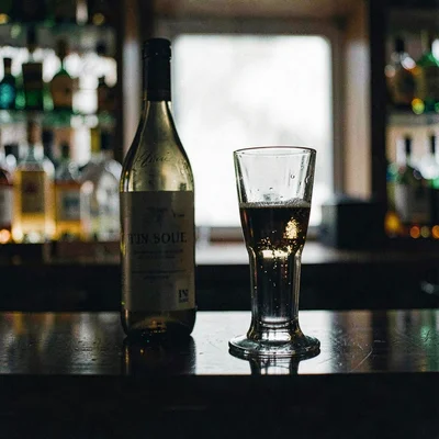 Bottle and a tall glass on a polished bar, lightbox-soft halo