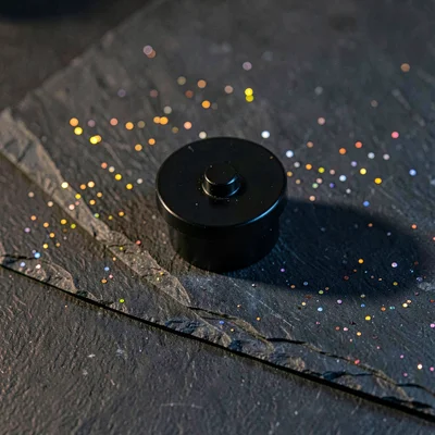 Onyx-black puck mount lying on cleaved slate, hairline mica flecks scattering pi