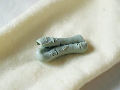 Snapped sage-green wishbone fragment with a thumb dent at the break and fingerna