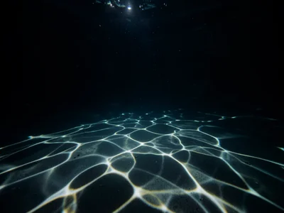 Flashlight underwater in dark pool, caustic light patterns on pool floor
