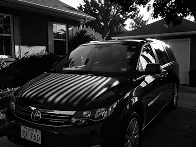 Minivan in driveway with venetian blind shadows striped across hood, hard mornin