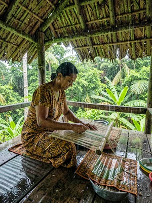 Open-air fale life in Samoa after rain, A woman weaving a mat in an open fale, r