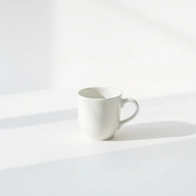 Minimalist photography of a single white coffee cup on a clean matte background, soft natural window light, subtle shado