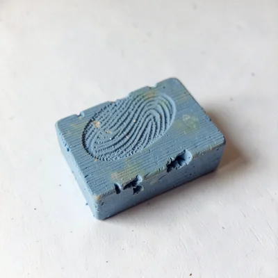 Etched faded-blue wooden block with thumb-pressed grain and fingernail dents alo