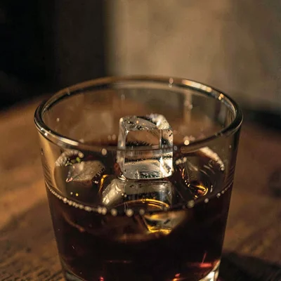 Moody close-up of a single ice cube clinking into a glass, low warm light