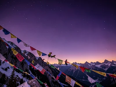 Prayer flags catching alpine wind against deepening violet sky