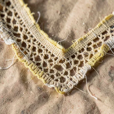 Worn-texture macro of an aged lace yoke with broken threads and yellowed cotton 