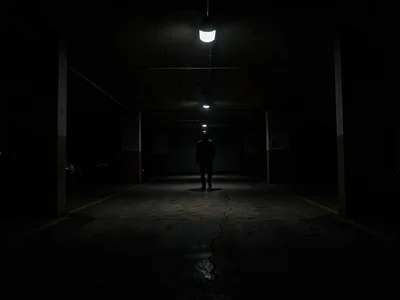 Figure at far end of parking garage, single overhead light creating pool, everyt