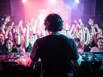 DJ booth from behind, hands on decks, crowd a blur of raised arms, everything pi