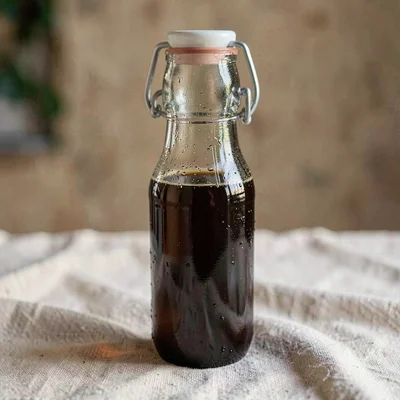 slim brown-glass bottle of cold-process kombucha with a swing-top cap, faint con