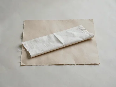 One unbleached linen napkin folded into a long rectangle on beige paper, edge fr