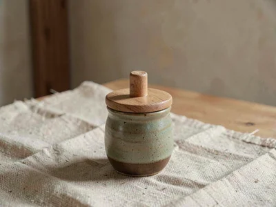 One small ceramic sugar pot with wooden lid and earthy glaze sitting central on