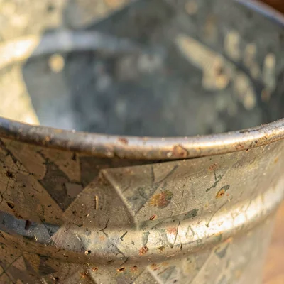 Mineral-cut close of a galvanized metal bucket rim, side-lit grain