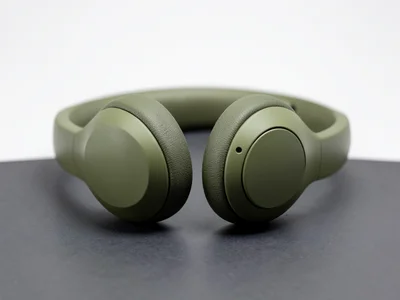 A pair of wireless headphones in matte olive, earcups showing texture, on a dark