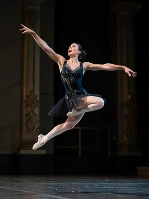 A ballet dancer frozen at the absolute peak of a leap, the moment before gravity